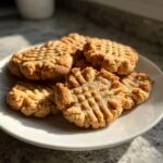 A close-up of golden brown 3 ingredient peanut butter cookies with classic fork marks on a white plate.
