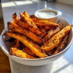 A bowl of perfectly crispy air fryer sweet potato fries with a small dish of dipping sauce.