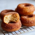 A close-up of a stack of apple cider donuts, with one donut broken in half to show the fluffy interior.