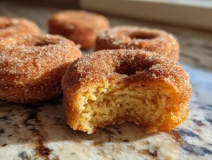 Close-up of a bite taken out of a perfectly baked apple cider donut, coated in cinnamon sugar.
