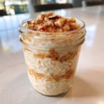 A close-up of apple cinnamon overnight oats in a mason jar, topped with chopped nuts and cinnamon.