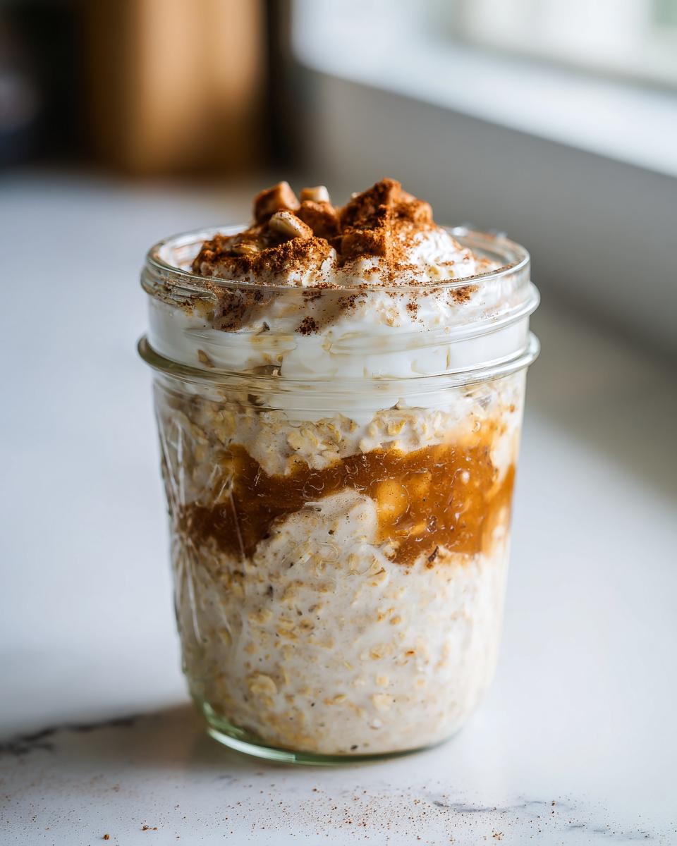 Close-up of apple cinnamon overnight oats in a mason jar, topped with yogurt and cinnamon.