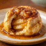 Close-up of a warm apple dumpling, with soft pastry and tender apple slices in a sweet, cinnamon-spiced syrup.