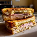 A close-up of an authentic Cuban sandwich, grilled to perfection, with layers of ham, turkey, pickles, and melted cheese.