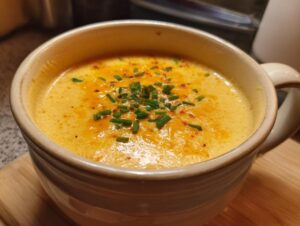 A close-up of a steaming mug of Amazing Beer Cheese Soup, garnished with fresh chives and a sprinkle of paprika.