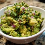 A close-up of the best guacamole, featuring chunky avocado, red onion, and fresh cilantro in a white bowl.