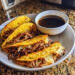 A plate of three golden-brown birria tacos filled with shredded meat and melted cheese, served with a side of consommé.
