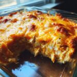 Close-up of a bubbly, cheesy Buffalo chicken dip in a glass baking dish, with a scoop removed.
