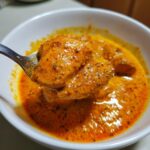 A spoonful of creamy, orange Butter Chicken with visible spices and tender chicken pieces.
