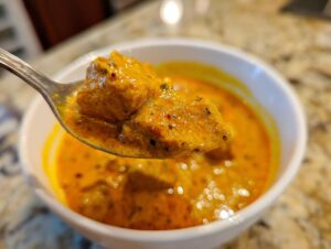 A close-up shot of tender chicken pieces coated in creamy orange butter chicken sauce on a spoon.