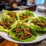 Close-up of fresh chicken lettuce wraps filled with seasoned ground chicken and topped with chopped green onions.