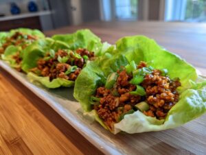 A close-up of several chicken lettuce wraps filled with seasoned ground chicken and topped with chopped green onions.