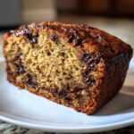 A close-up of a slice of moist chocolate chip banana bread on a white plate.