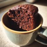 A close-up of a moist chocolate mug cake with a bite taken out, served in a mug.