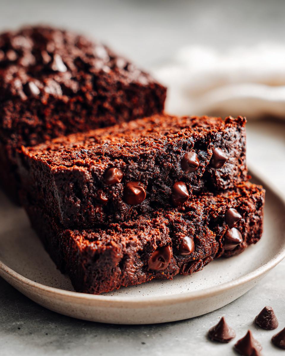 Close-up of two moist slices of chocolate zucchini bread, studded with chocolate chips, on a plate.