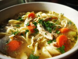 Close-up of a comforting bowl of classic chicken noodle soup with shredded chicken, noodles, carrots, and parsley.