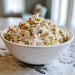 A white bowl filled with creamy Classic Tuna Salad mixed with chopped celery.