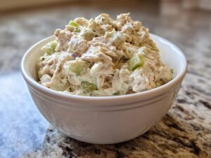 A white bowl filled with creamy Classic Tuna Salad, featuring chunks of tuna, celery, and herbs.