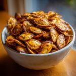 A close-up of a bowl filled with perfectly roasted pumpkin seeds, glistening and golden brown.