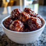 A white bowl filled with glistening Crockpot BBQ meatballs coated in a rich, dark sauce.
