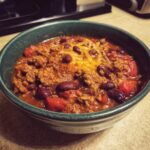 A close-up of a bowl of delicious Crockpot chili, featuring ground beef, kidney beans, tomatoes, and melted cheese.