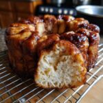 A close-up of a freshly baked Monkey Bread loaf on a cooling rack, with a piece pulled out to show the fluffy interior.