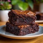 Two stacked fudgy chocolate brownies on a plate, showcasing their rich texture and glossy tops.