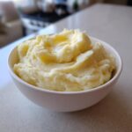 A close-up of fluffy Garlic Mashed Potatoes in a white bowl, topped with melted butter.
