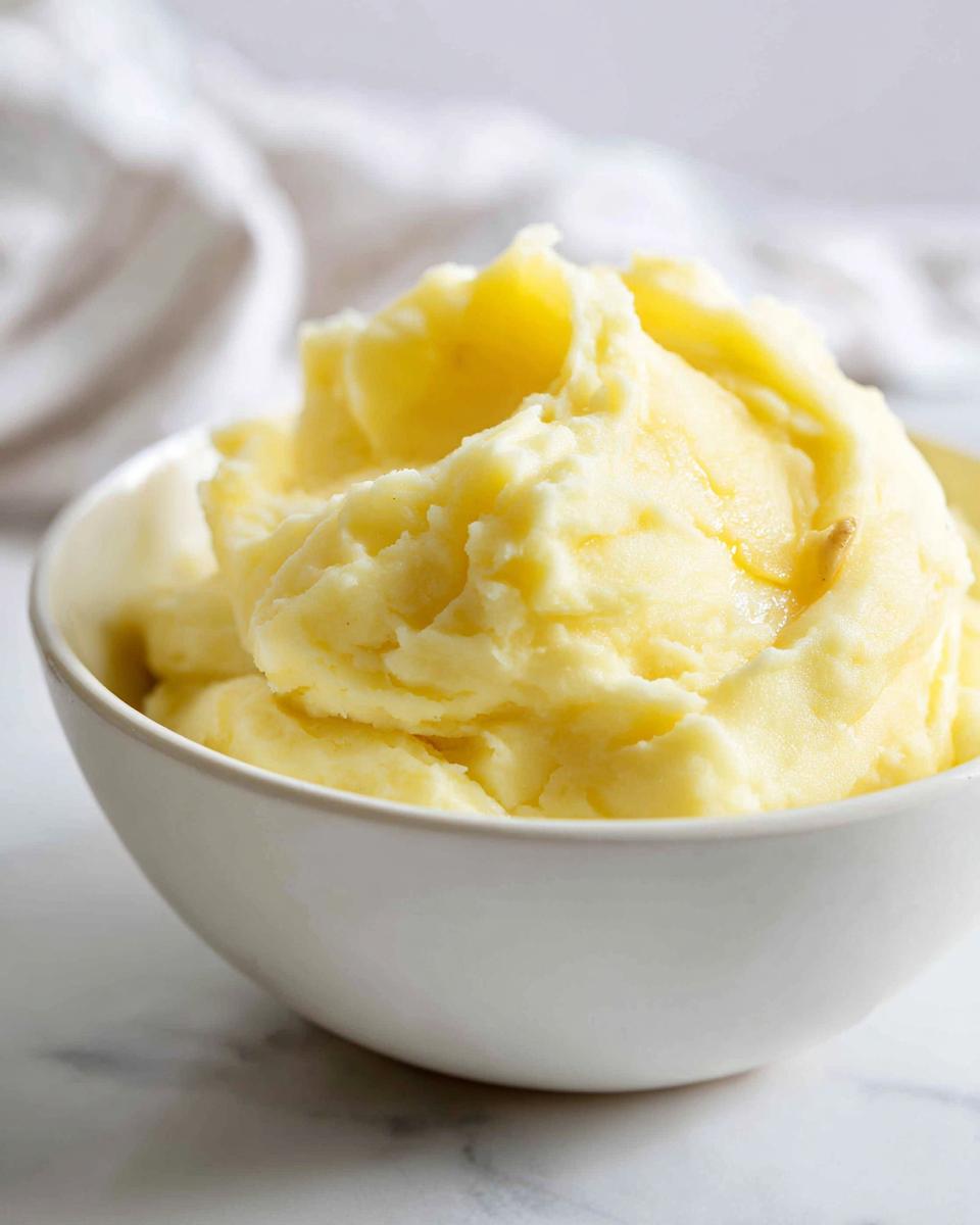 A close-up of fluffy garlic mashed potatoes in a white bowl, topped with melted butter.