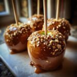 Close-up of a glossy caramel apple covered in chopped nuts on a stick.