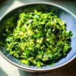 A close-up of a vibrant Green Goddess Salad in a blue bowl, packed with fresh greens and creamy avocado.