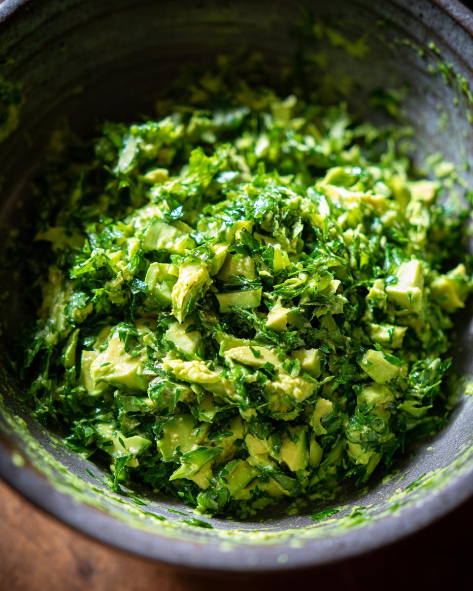 Close-up of a bowl filled with a vibrant Green Goddess Salad, featuring chopped avocado and fresh herbs.