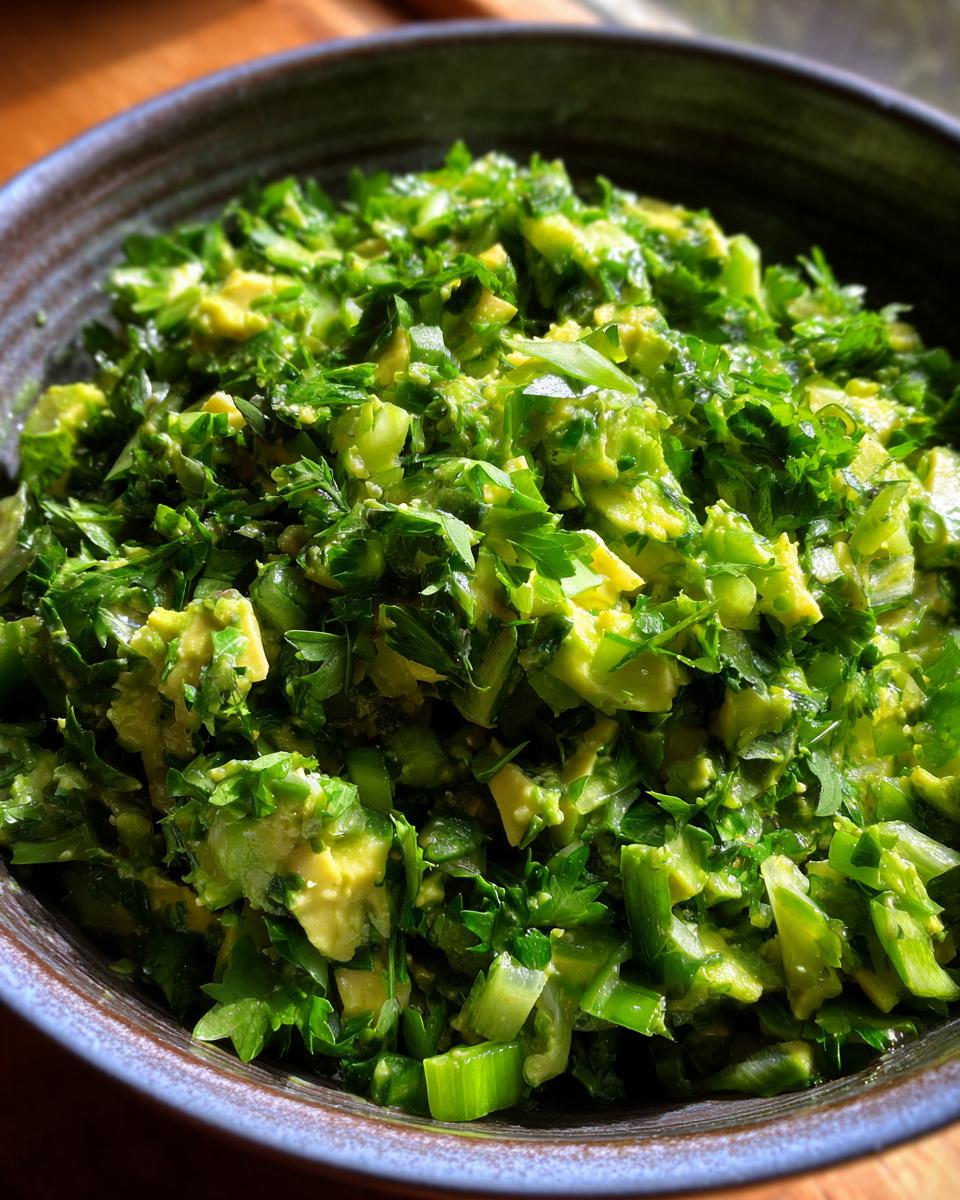 Close-up of a bowl filled with vibrant Green Goddess Salad, featuring chopped avocado, celery, and fresh parsley.