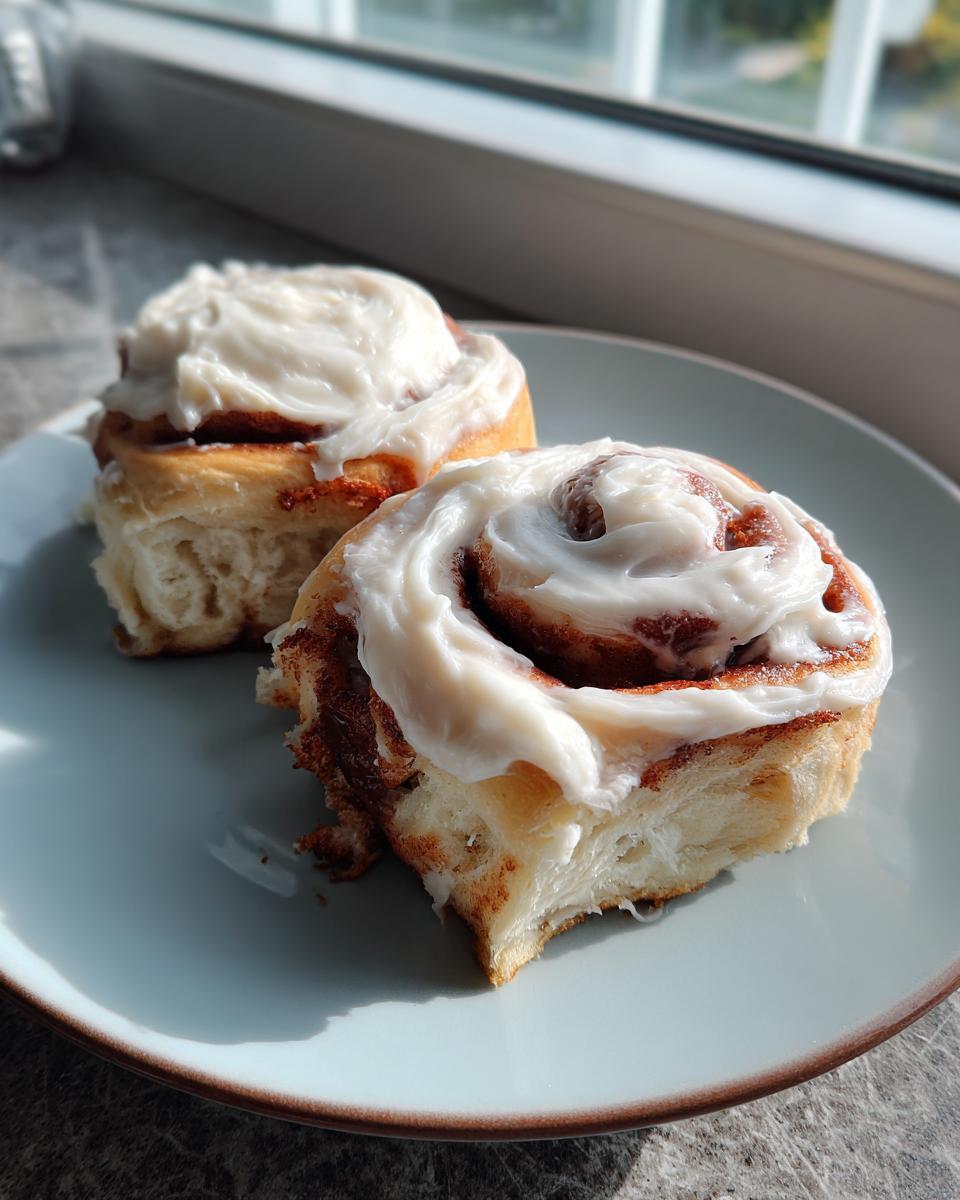 Two delicious homemade cinnamon rolls generously topped with creamy frosting on a light blue plate.