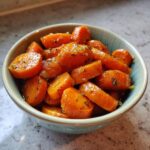 A close-up shot of a bowl filled with glistening honey glazed carrots, sprinkled with herbs.