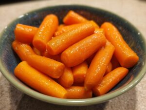 Close-up of bright orange baby carrots glazed with honey in a blue-green bowl.
