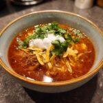 A close-up of a bowl of Instant Pot chicken tortilla soup topped with sour cream, cilantro, and tortilla strips.