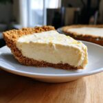 A close-up of a slice of lemon icebox pie with a graham cracker crust, topped with lemon zest.