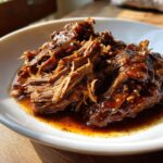 Close-up of a bowl filled with shredded Mississippi pot roast in a rich, glossy sauce.