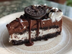 A decadent slice of no-bake chocolate lasagna, layered with chocolate mousse, cream, and crushed Oreos, topped with a whole Oreo and chocolate drizzle.