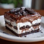 A decadent slice of no-bake chocolate lasagna with layers of chocolate pudding, whipped cream, and crushed Oreos.