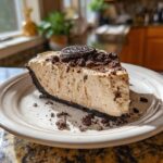 A delicious slice of no-bake peanut butter pie topped with crushed Oreos and a whole Oreo.