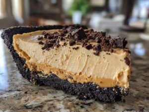 Close-up of a slice of no-bake peanut butter pie with a chocolate crust and crushed cookies on top.