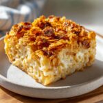 A close-up of a slice of Noodle Kugel on a plate, featuring a creamy noodle base and a crunchy, caramelized cornflake topping.