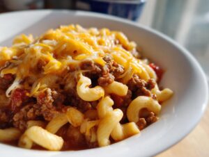 A close-up of a bowl of one pot chili mac, featuring elbow macaroni, seasoned ground beef, and melted cheddar cheese.