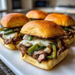 Close-up of four delicious Philly cheesesteak sliders with steak, peppers, onions, and melted cheese on toasted buns.