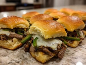 Close-up of several Philly cheesesteak sliders with melted cheese, steak, and green peppers.