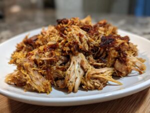 Close-up of a pile of tender and crispy pork carnitas on a white plate, ready to be served.