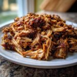 A close-up of a pile of shredded pork carnitas on a white plate, glistening and browned.