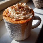 A close-up of a creamy Pumpkin Spice Latte topped with whipped cream and a sprinkle of cinnamon in a textured white mug.